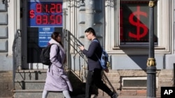 Oamenii trec pe lângă ecranul unei case de schimb valutar care afișează ratele de schimb ale dolarului american față de rubla rusească în Sankt Petersburg, Rusia, în aprilie 2023.
