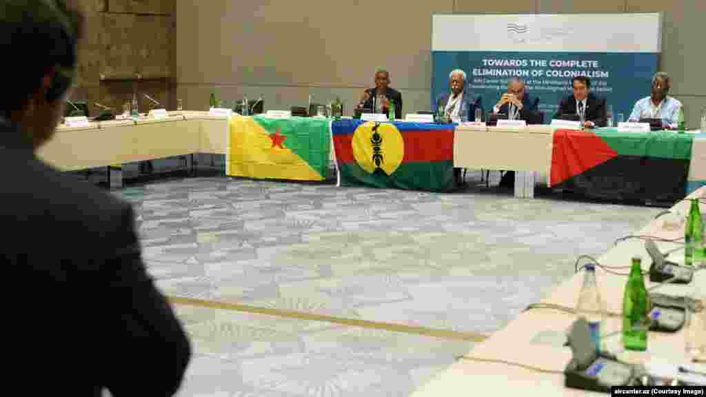 Azerbejdžanske zastave počele su se pojavljivati u Novoj Kaledoniji ubrzo nakon što su politički aktivisti sa nekoliko francuskih teritorija prebačeni u Baku na konferenciju pod nazivom "Ka potpunoj eliminaciji kolonijalizma", u julu 2023. Na ovoj fotografiji sa događaja, govornici sjede iza zastava koje se koriste na francuskim teritorijama (slijeva nadesno) Francuske Gvajane, Nove Kaledonije i Martinika. 