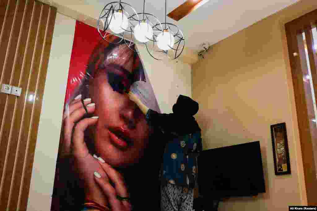 An Afghan beautician removes a poster in a beauty salon in Kabul on July 24 after it was forced to close by Taliban decree. The closure has sparked rare public opposition from many Afghan women as it leaves another hole in their economic and social lives. 