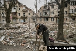 Un bătrân adună lemne din dărâmături în fața unui bloc de apartamente distrus în Avdiivka, în martie 2023.