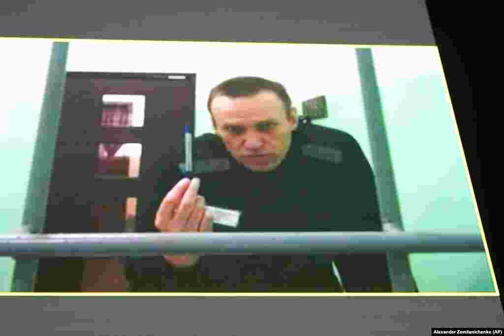 Лидер российской оппозиции Алексей Навальный на экране телевизора по видеосвязи, предоставленной ФСИН России из колонии в Мелехово Владимирской области, во время слушаний в Верховном суде России в Москве. Россия, 22 июня. Навальный подал иск, оспаривая тюремные правила, которые, по его словам, позволяют тюремным чиновникам лишать его канцелярских принадлежностей и ручек, тем самым нарушая его право подавать на них жалобы. (AP Photo/Alexander Zemlianichenko)
