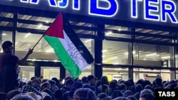 Un bărbat flutură un steag palestinian pe care scrie „Daghestan este alături de tine” în timpul unui miting pro-palestinian la aeroportul din Mahacikala, după sosirea unui zbor de linie de la Tel Aviv, pe 29 octombrie.