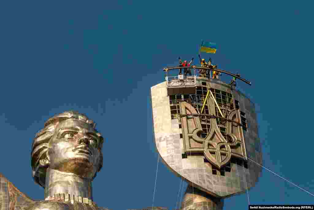6 august 2023. Muncitorii se bucură după instalarea tridentului ucrainean pe Monumentul Patriei de la Kiev. Tridentul înlocuiește stema sovietică.