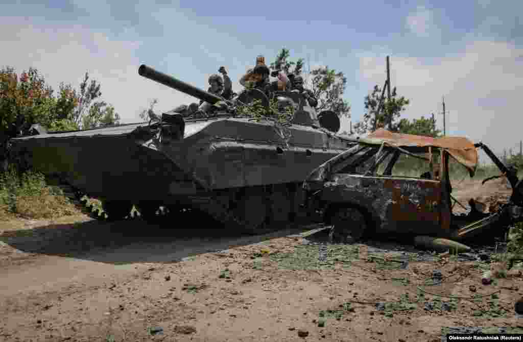 Украинские военные проезжают на БМП мимо разрушенной машины 