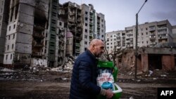 Човек носи тоалетна за домашни любимци на фона на засегната от обстрел жилищна сграда в Чернигов. Снимката е илюстративна