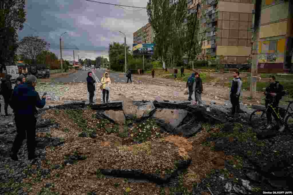 Жители смотрят на воронку, образовавшуюся после ракетного удара по Днепру, 10 октября. Президент России Владимир Путин назвал ракетные удары «ответом» на взрыв на Крымском мосту 8 октября. Мост соединяет Россию с аннексированным в 2014 году полуостровом Крым 