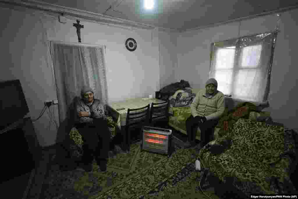 Two elderly women warm themselves near a heater in Stepanakert. 