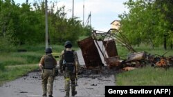 Українські військові йдуть біля знищеної військової машини в селі Руська Лозова, на Харківщині, Україна, 28 травня 2022 року. Фото ілюстративне