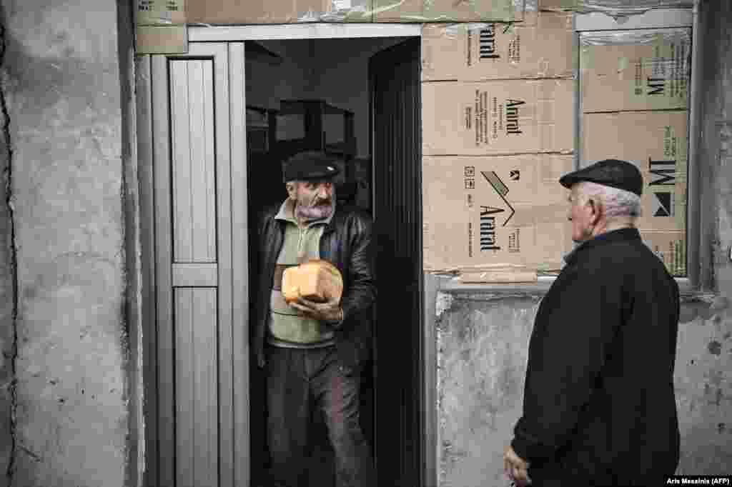 A man emerges from the bakery with fresh loaves of bread. 