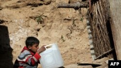 A Pakistani boy drinks water from a gallon container outside his makeshift tent in an Islamabad slum.