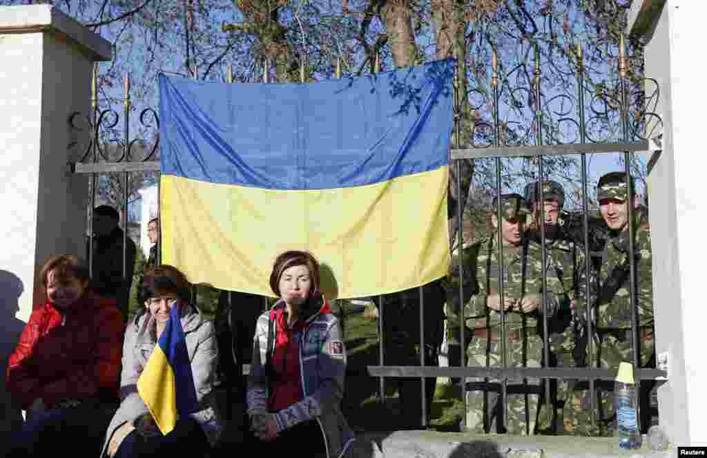 У селищі Любимівка українські військовослужбовці збираються на території військової частини. Їхні родичі сидять біля паркану, щоб не допустити збройних зіткнень. 3 березня 2014 року