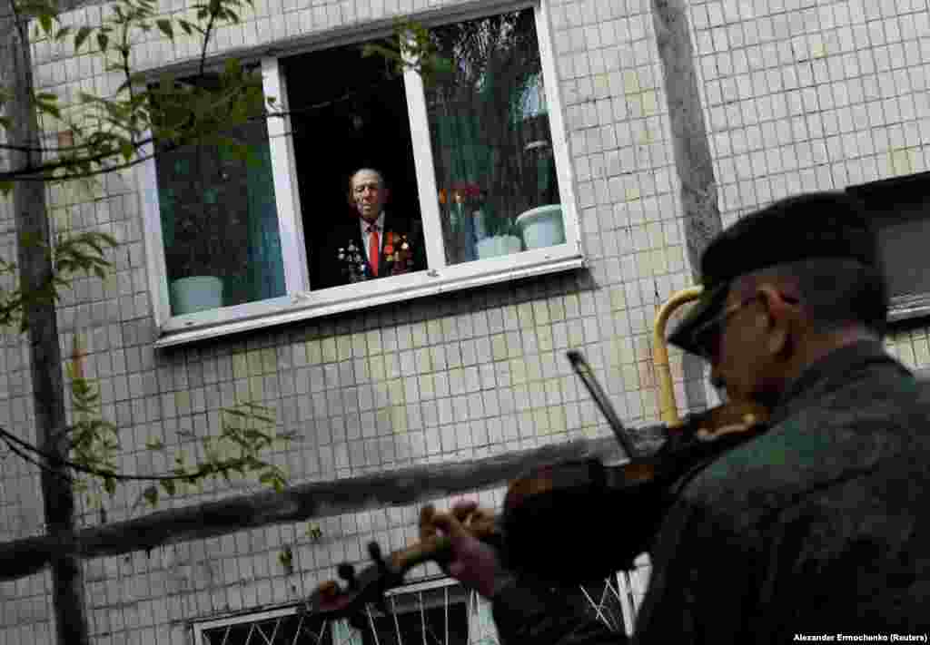 Veteran iz Drugog svetskog rata, star 96 godina, sa prozora svog stana, gleda bend koji svira tokom proslave Dana pobede, 9. maja, u Donjecku u Ukrajini.