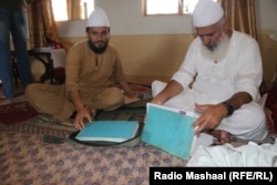 میا محمد جاوېد مېټا (ښي خوا ته) له خپل زوی میا نور محمود سره ناست دی او د نویو مسلمانو شویو کسانو رجسټر ګوري.