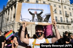 Demonstrant drži plakat na kojem se vidi kako mađarski premijer Viktor Orban drži šal u duginim bojama, ispred zgrade parlamenta u Budimpešti u junu 2021. tokom demonstracija protiv vladinog nacrta zakona kojim se želi zabraniti "promocija" homoseksualnosti i promjene spola.