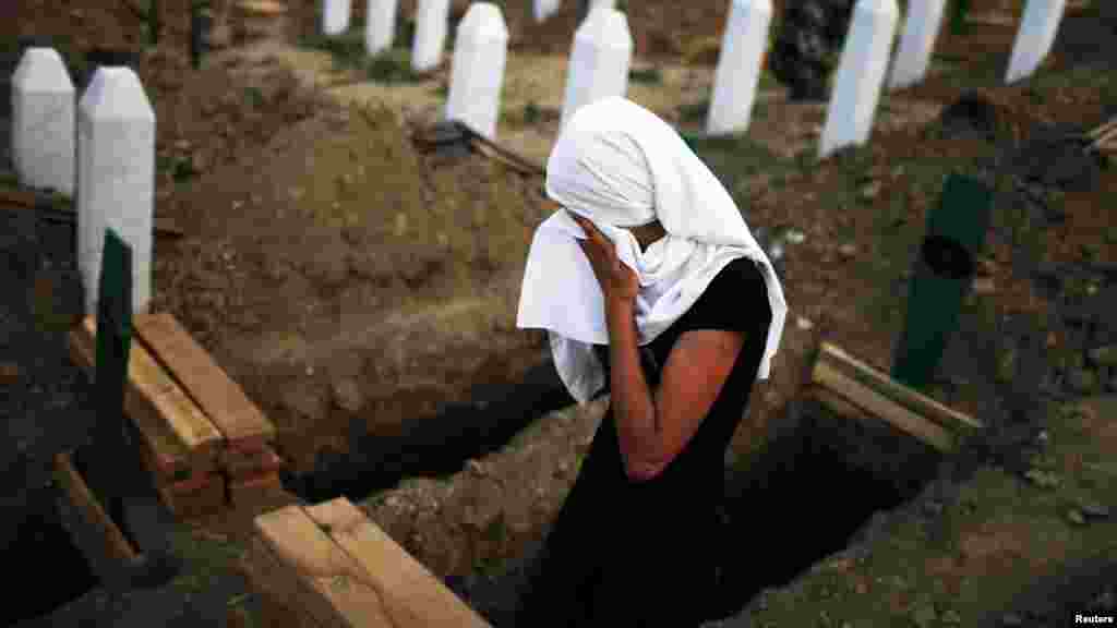 A woman cries near a new open grave with the coffin of her late relative's remains, prepared for burial on July 11.