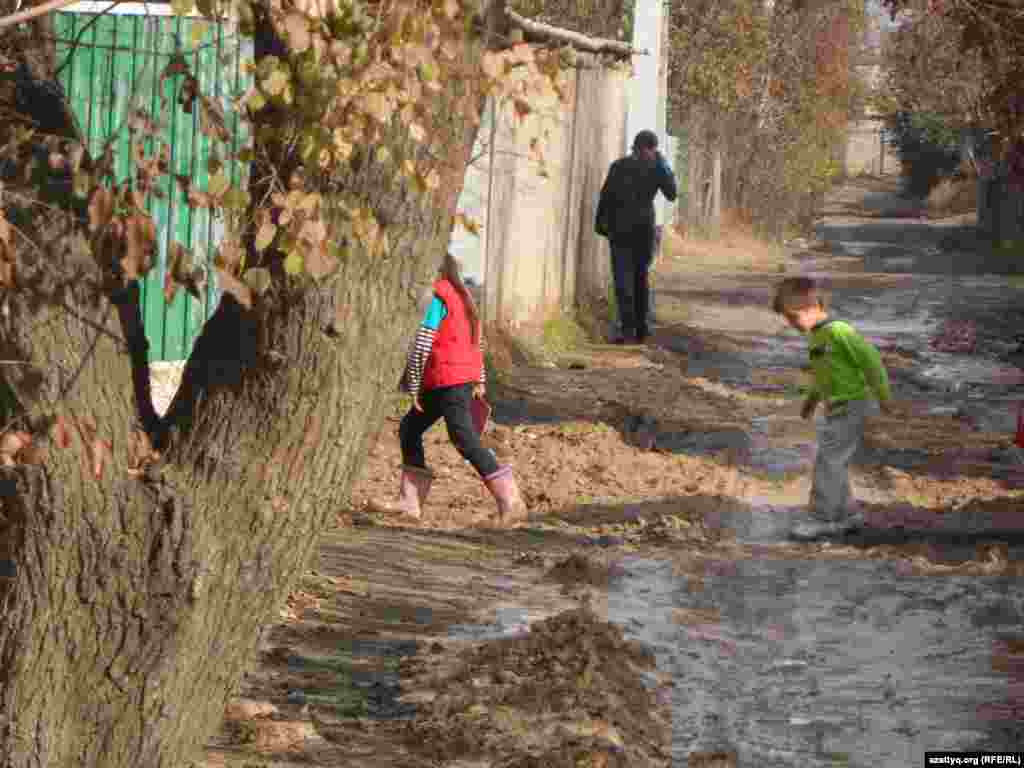 Дети переходят утопающую в грязи дорогу.