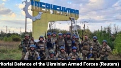 Soldații ucraineni s-au fotografiat la semnul care indică intrarea în orașul Șevcenkove, regiunea Harkov. Imagine din 10 septembrie 2022. Imagini cu drapelul ucrainean care flutură în mai multe orașe recucerite au apărut pe rețelele de socializare.