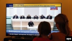 Женщина с ребенком смотрит телевизор во время трансляции программы о заседании Совета Федерации России, на котором обсуждается вопрос об использовании российских войск в Украине. 1 марта 2014 года.