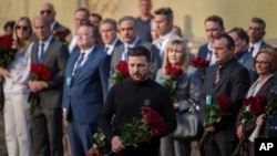 Ukrainian President Volodymyr Zelenskyy places flowers on the wall of a house destroyed by an April 24 Russian strike on a residential neighborhood of Kyiv that killed 12 people.