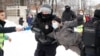 Un bărbat care poartă o vestă de presă întinde un microfon în timp ce poliția reține un protestatar în timpul unui miting împotriva arestării lui Alexei Navalnîi