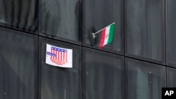 یک پوستر ضدآمریکایی در کنار پرچم جهوری اسلامی بر یک ساختمان دولتی در تهران، آبان ۱۴۰۲