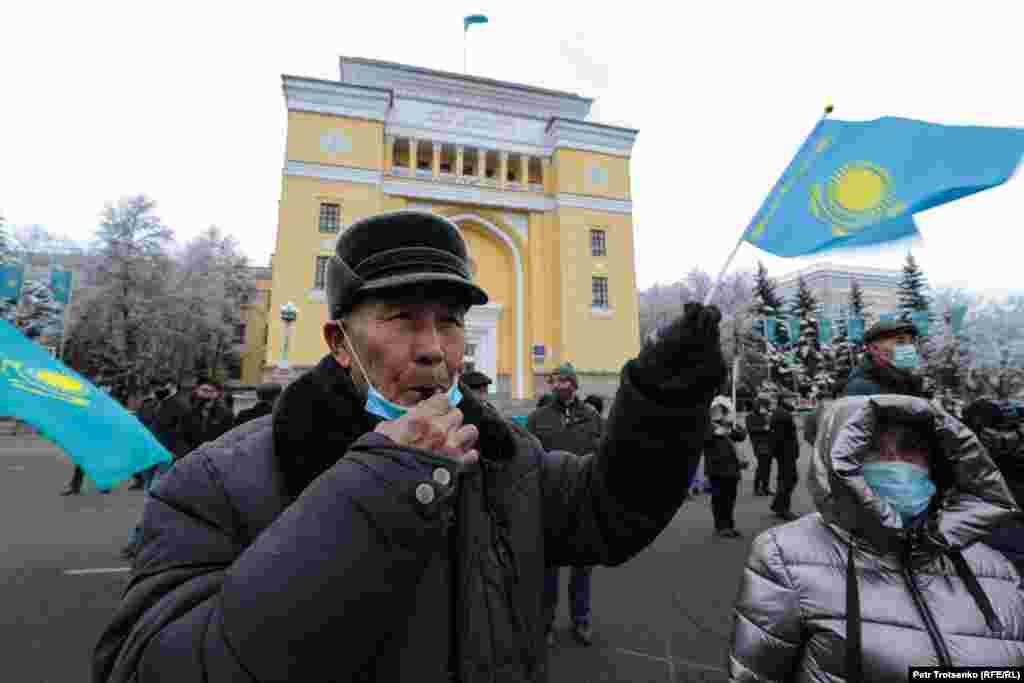 Мужчина с казахстанским флажком в руках дует в свисток, таким образом выражая согласие со словами выступающих активистов.