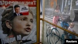 A woman pushes a child on a stroller past an advertisement for a magazine with presidential candidate Yulia Tymoshenko on the cover and an election sticker for current incumbent Petro Poroshenko.