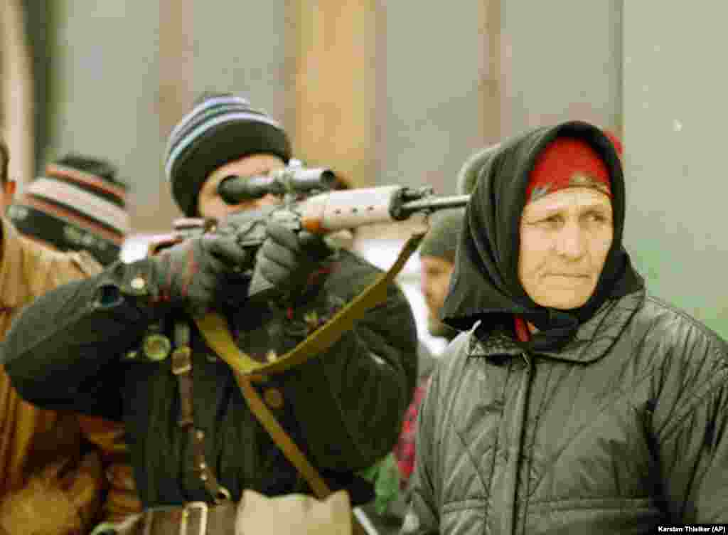 Čečenski snajperista cilja, dok žena pazi odakle može da dođe ruski snajper u blizini ulične pijace u predgrađu Groznog, 25. januar 1995.