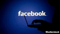 Georgia -- A woman works on his computer in front of Facebook sign

