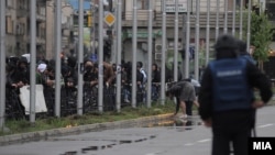 A mourner lights a candle for the victims of the Smiljkovci murders as security forces look on in Skopje on April 16.