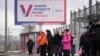 Oamenii așteaptă într-o stație de autobuz din Sankt Petersburg lângă un panou publicitar care promovează viitoarele alegeri prezidențiale din Rusia.