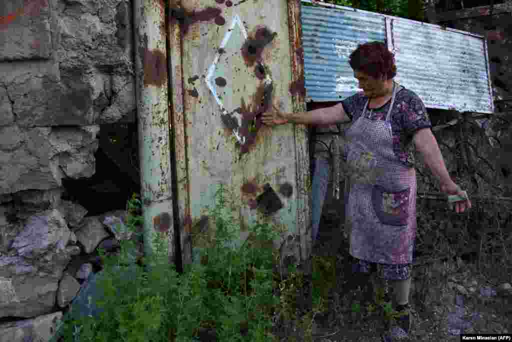 A woman in the Armenian village of Aygepar shows how the gate to her yard was damaged by shelling.