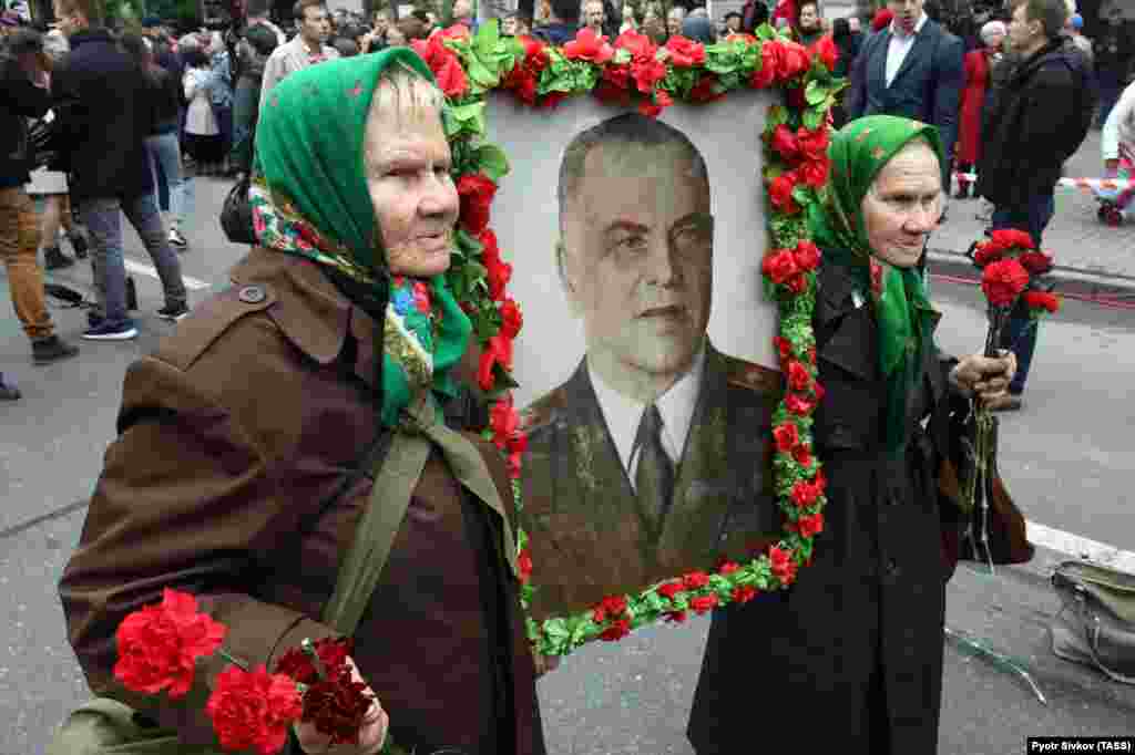 Două veterane din al doilea război mondial poartă portretul Mareșalului Ghenadi Jukov, o figură emblematică a Armatei Roșii, la Ziua Victoriei celebrată la Kiev, 9 Mai. (TASS/Pyotr Sivkov)