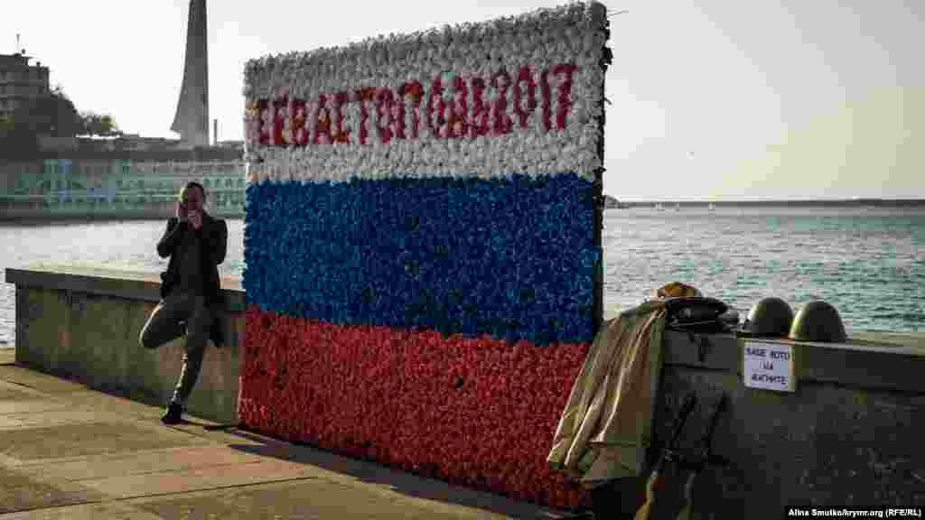 Мужчина поджидает туристов, чтобы сфотографировать на фоне триколора «Севастополь»